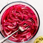 A glass bowl with marinated pink Mexican Pickled Onions with a squeezed lime to the side.