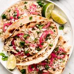 Salsa Verde Chicken tacos with limes, crumbled cheese, and pickled onions to the side.
