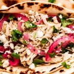 Close up of chicken tacos topped with cilantro, crumbled white cheese, and pickled red onions.