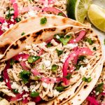 Salsa Verde Chicken tacos with limes, crumbled cheese, and pickled onions to the side.