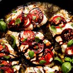 Skillet of chicken covered in mozzarella cheese and topped with tomatoes, basil, and balsamic glaze.