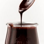 Lifting a spoon out of a jar of Chocolate Syrup.