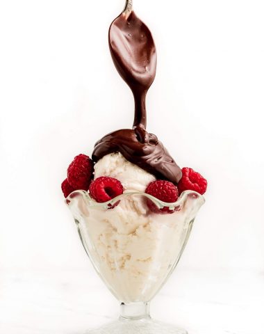 Drizzling hot fudge sauce over a cup of ice cream and raspberries.