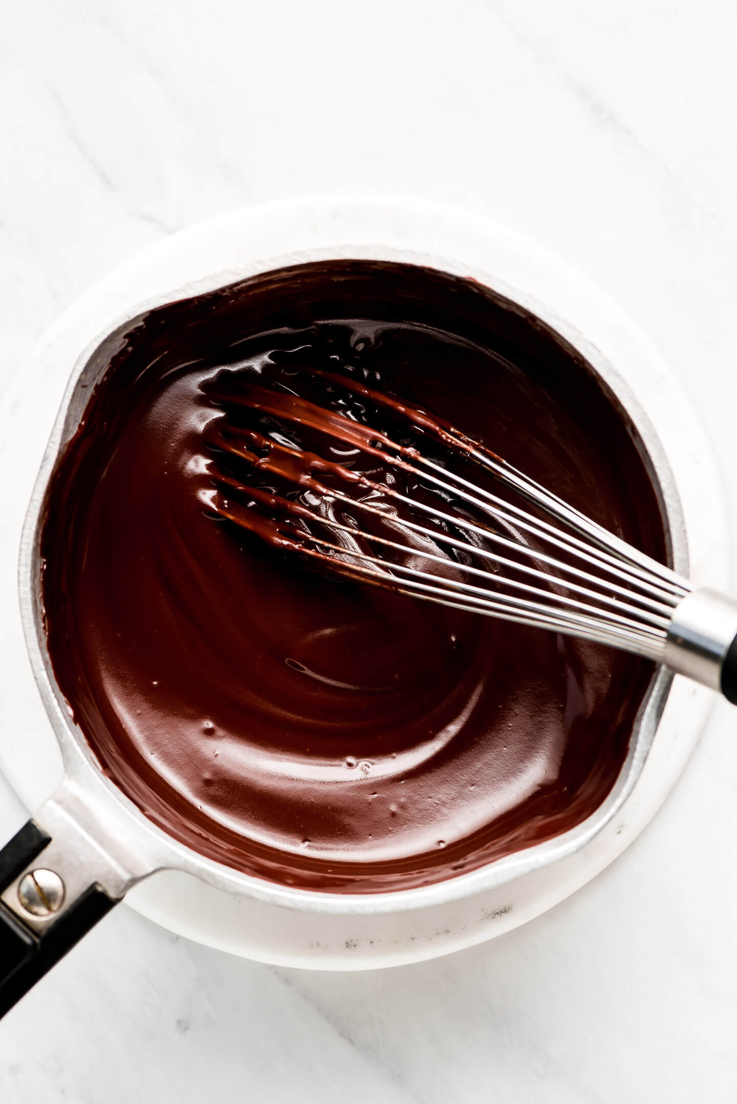 A whisk in a pot of hot fudge sauce.