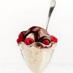 A glass dish of vanilla ice cream with raspberries, covered in hot fudge.