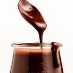 A spoon lifting out chocolate hot fudge our of a jar.