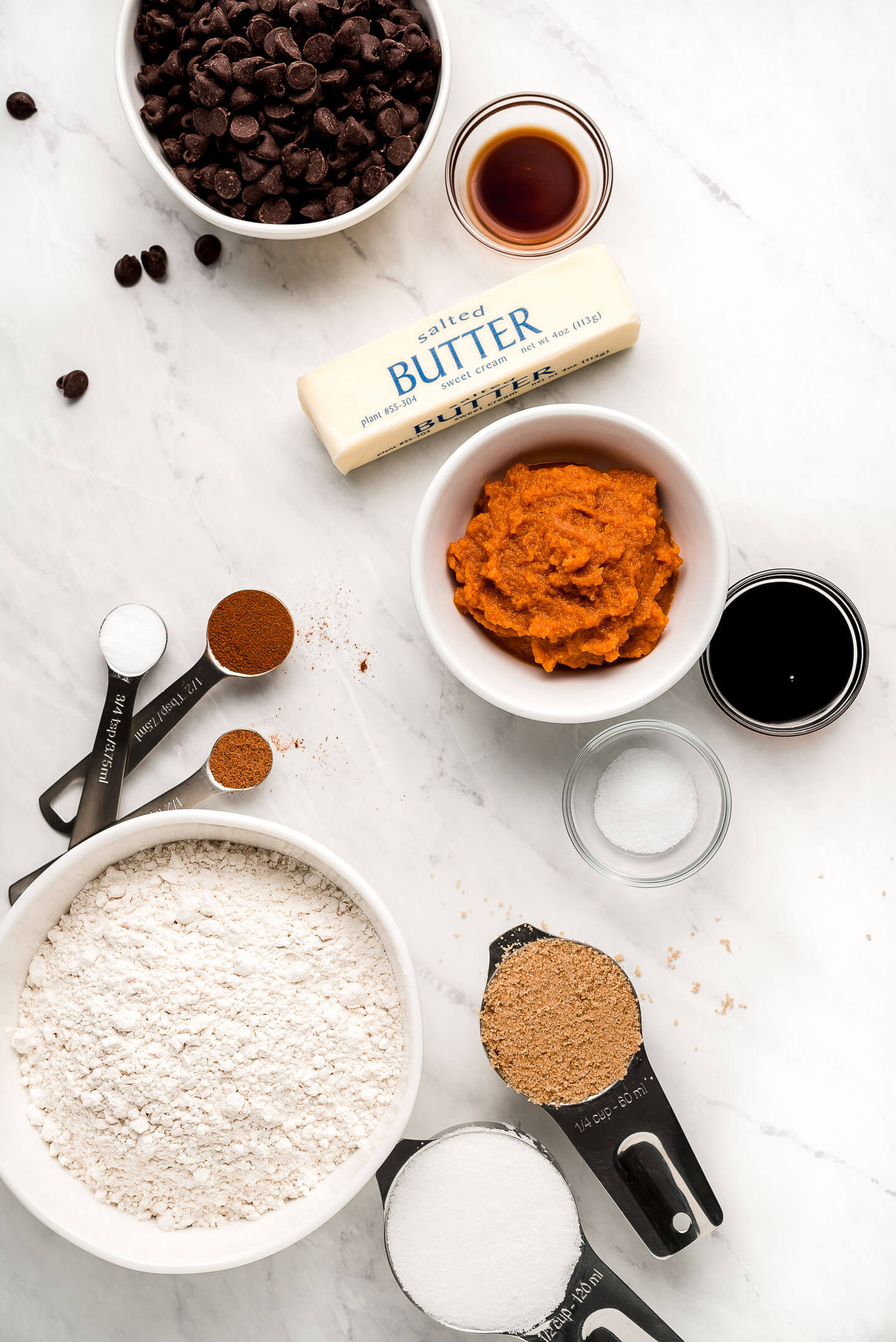 Ingredients on a marble surface- chocolate, vanilla, butter, pumpkin, sugar, flour, and spices.