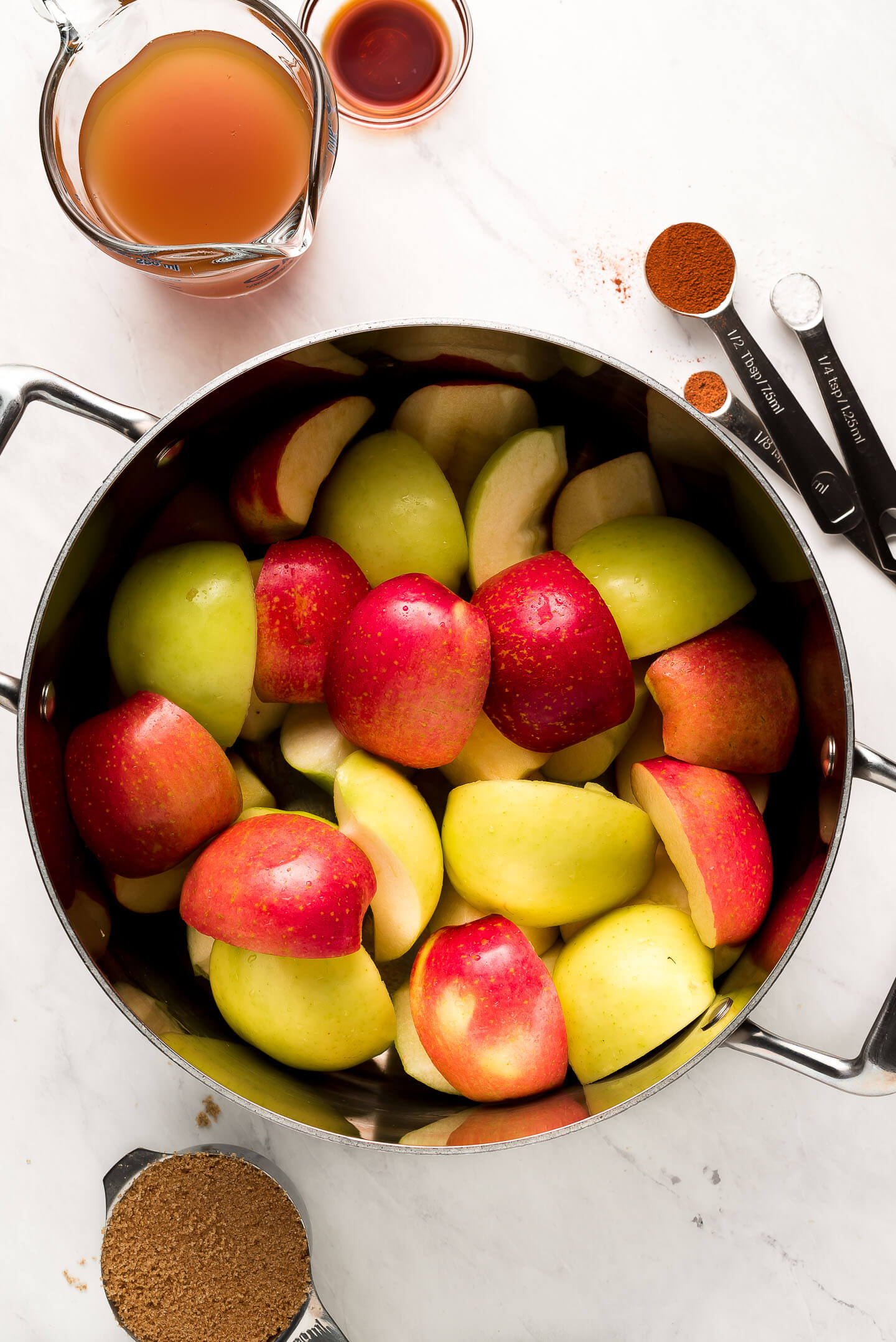 Quartered apples in a pot with ingredients surrounding.