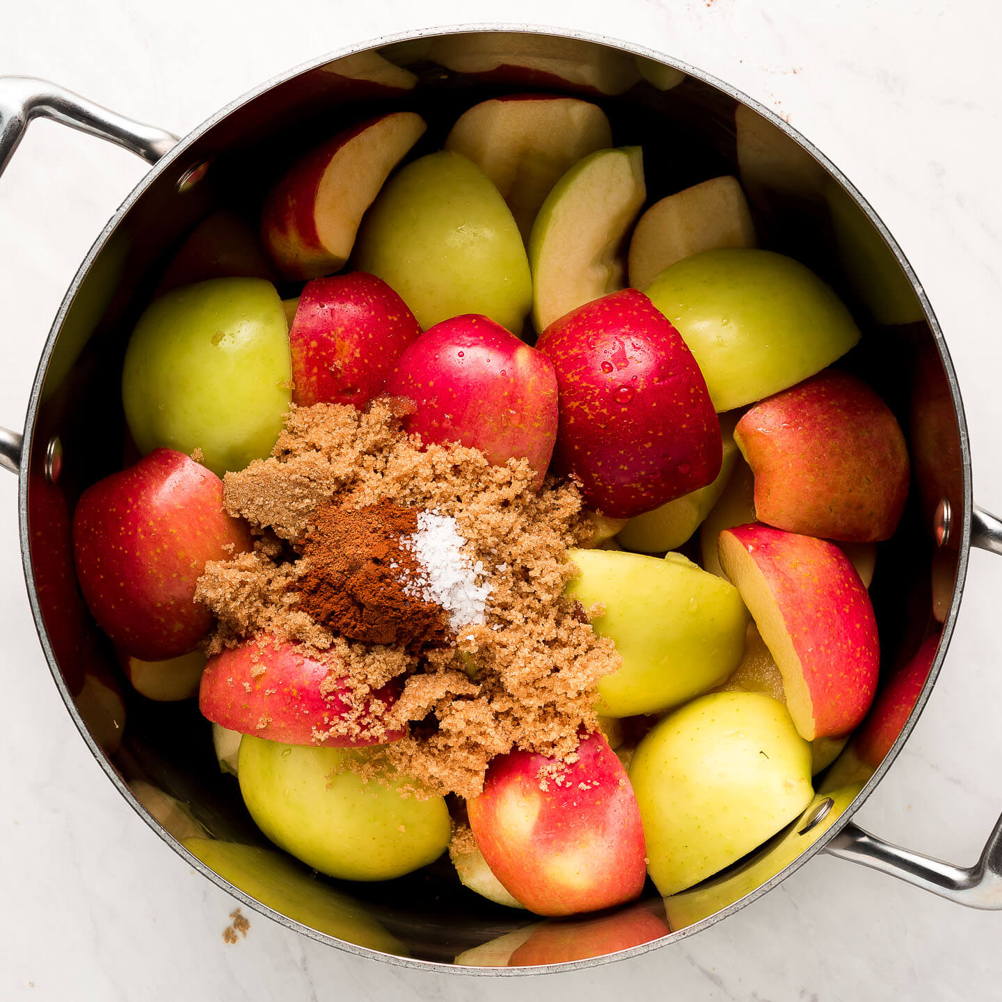 Apple quarters in a pot with sugar and spices.