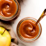 Apple butter in jars with apples to the side.