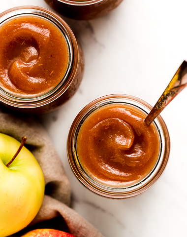 Apple butter in jars with apples to the side.