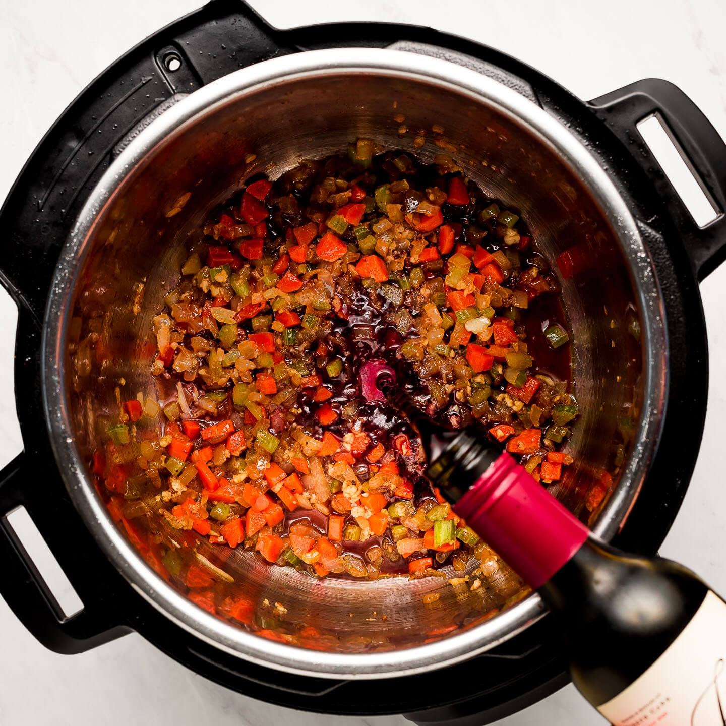 Pouring wine into an Instant Pot of cooked vegetables.