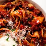 Beef Ragu in a bowl topped with ricotta, parmesan, and parsley.
