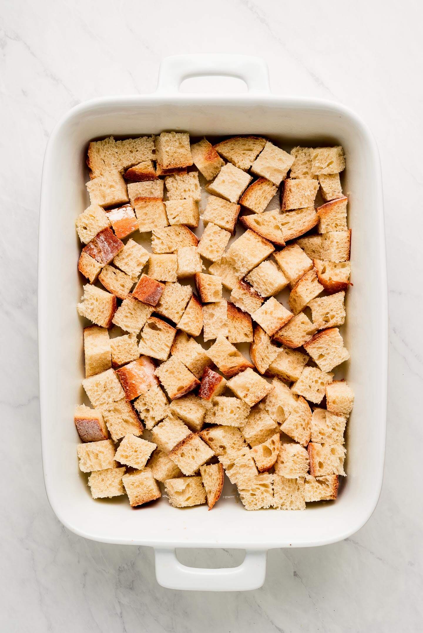 A white baking dish with cubes of bread in the bottom.
