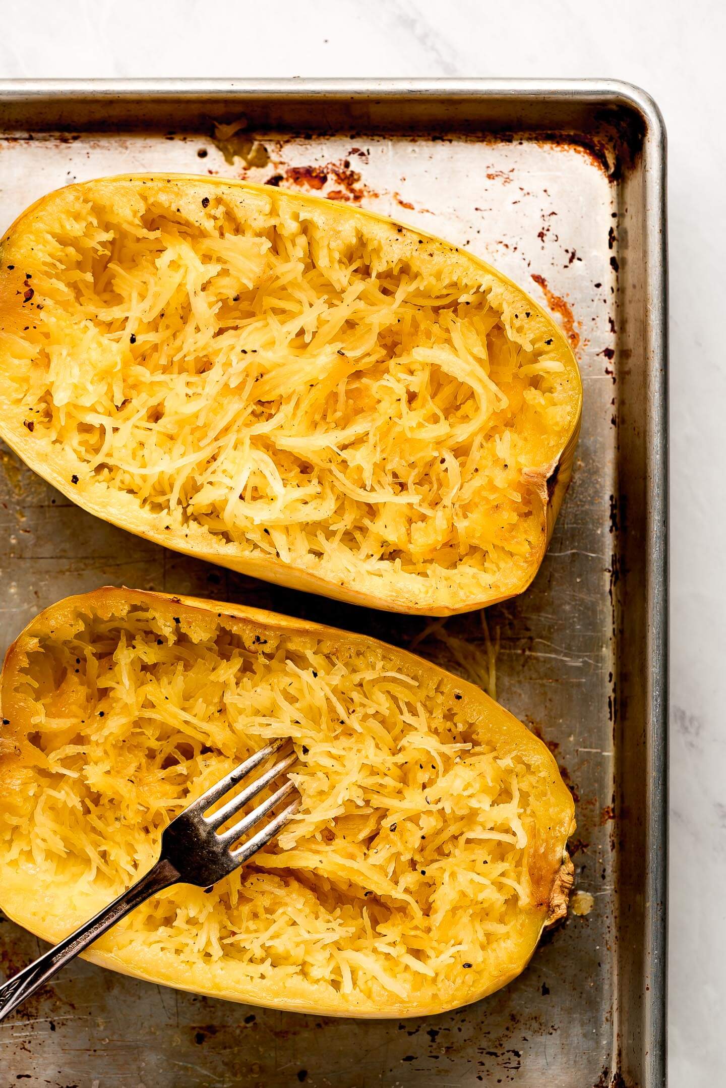 Two halves of spaghetti squash fluffed with a fork.