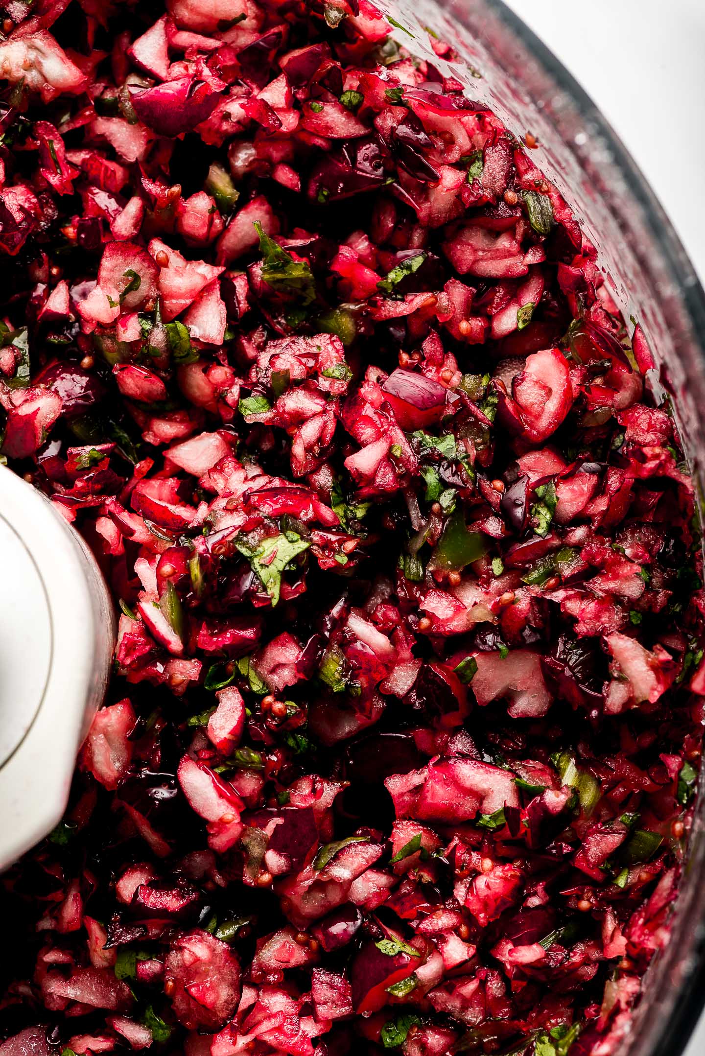 Close up of cranberries and cilantro chopped up in a food processor.