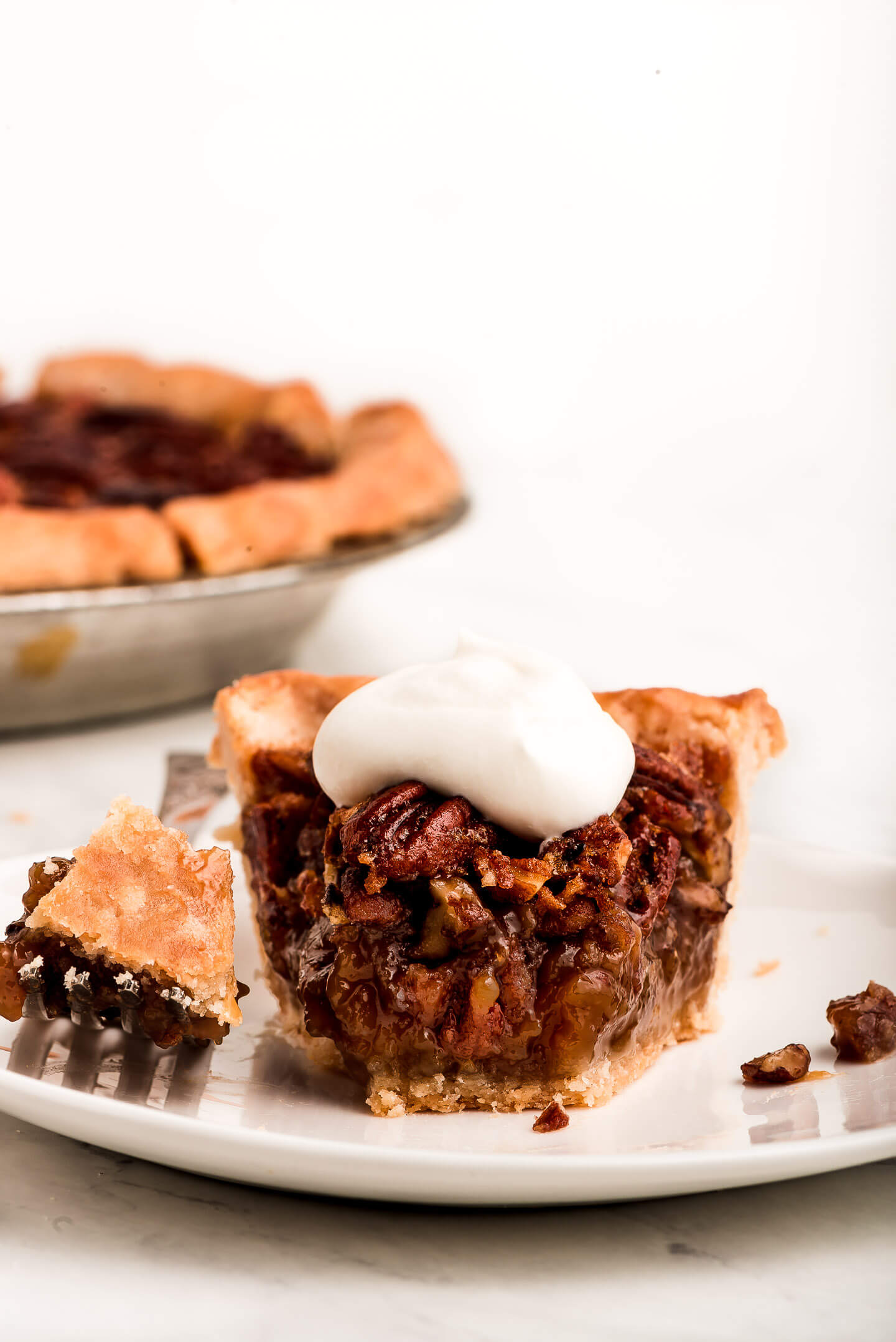 A slice of Pecan Pie with whipped cream and a bit taken out on a fork to the side.