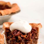 A slice of Pecan Pie with whipped cream and a bit taken out on a fork to the side.