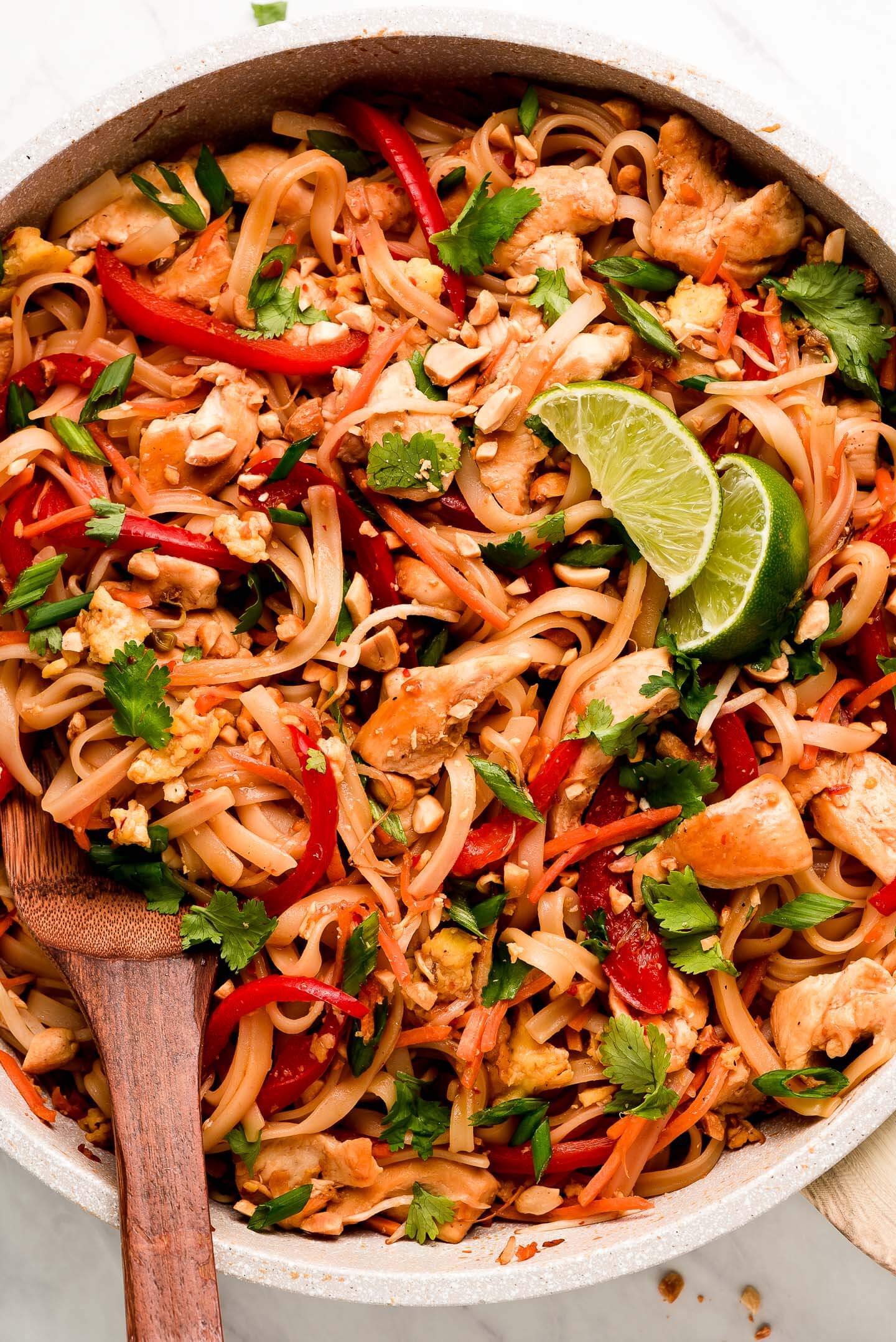 A skillet of Chicken Pad Thai with cilantro, peanuts, red peppers, and carrots.