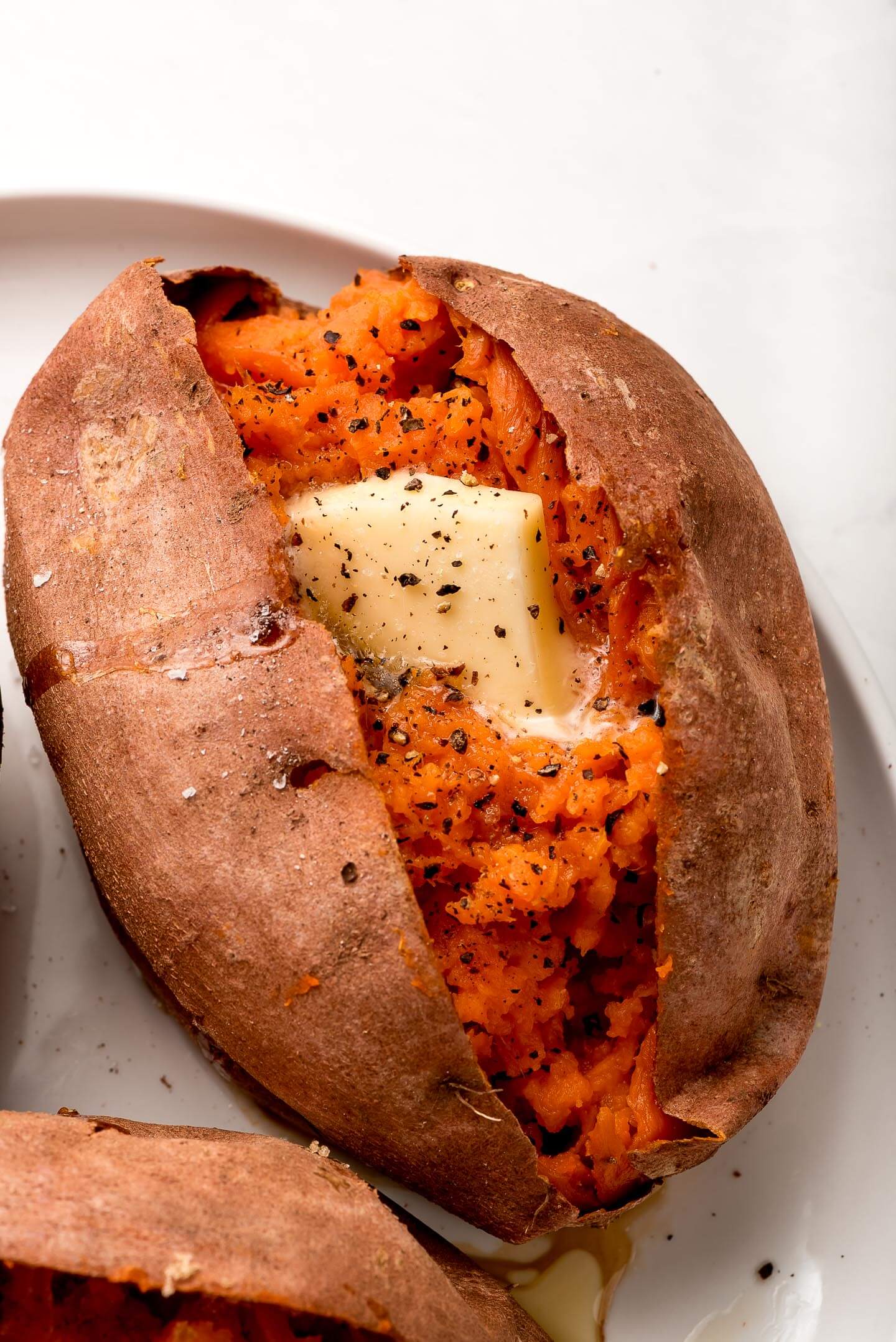 Close up of a baked sweet potato, cut open and topped with butter and salt & pepper.