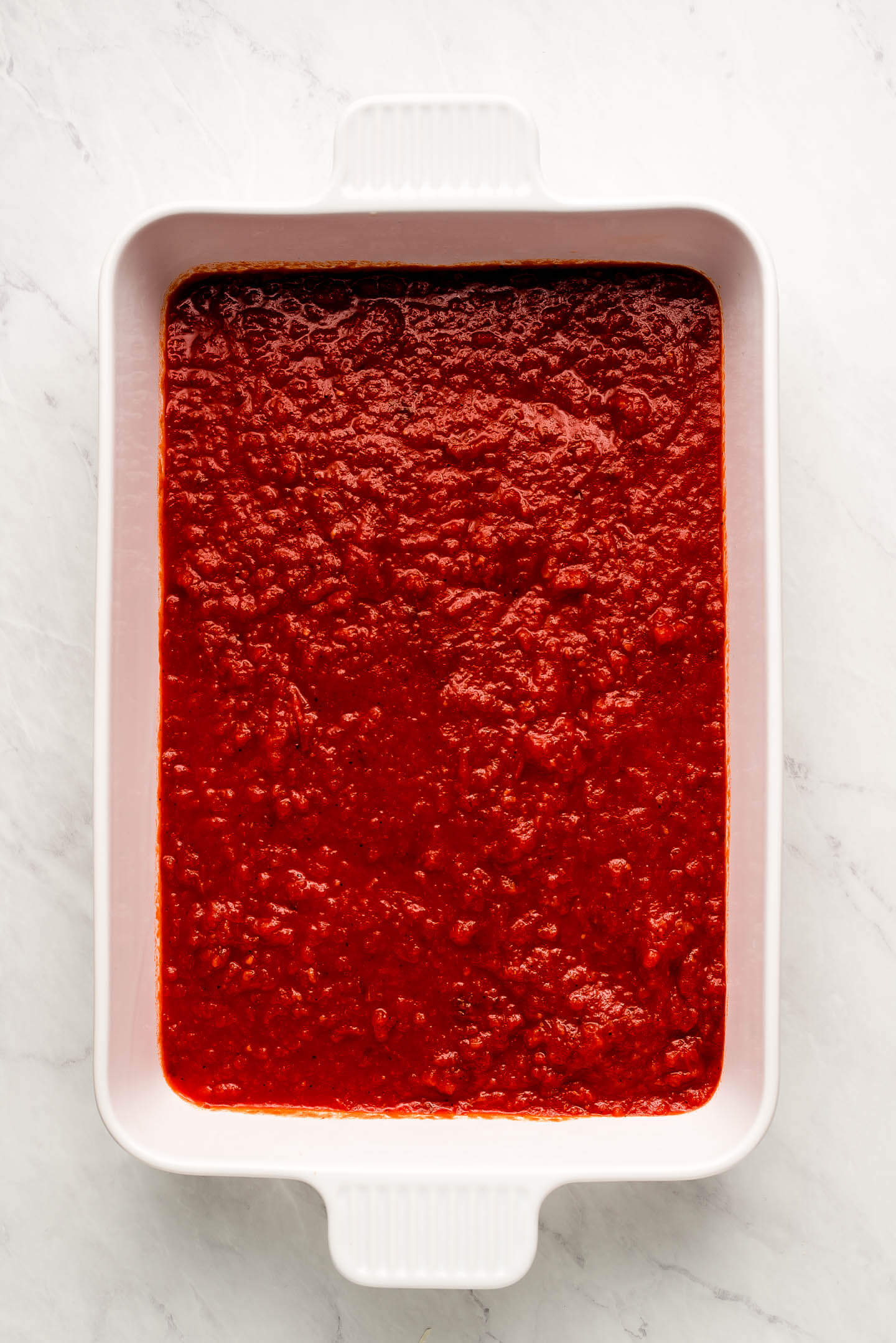 A white casserole dish with red marinara sauce on the bottom.