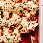 White baking dish with Stuffed Shells topped with cheese and parsley.