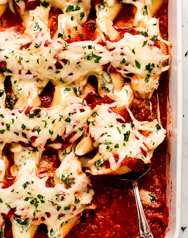 White baking dish with Stuffed Shells topped with cheese and parsley.